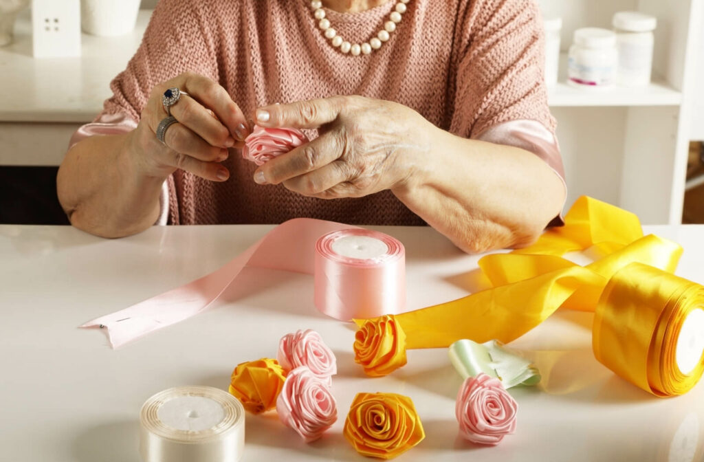 An older adult making handcrafted roses out of differently-colored lengths of ribbon.