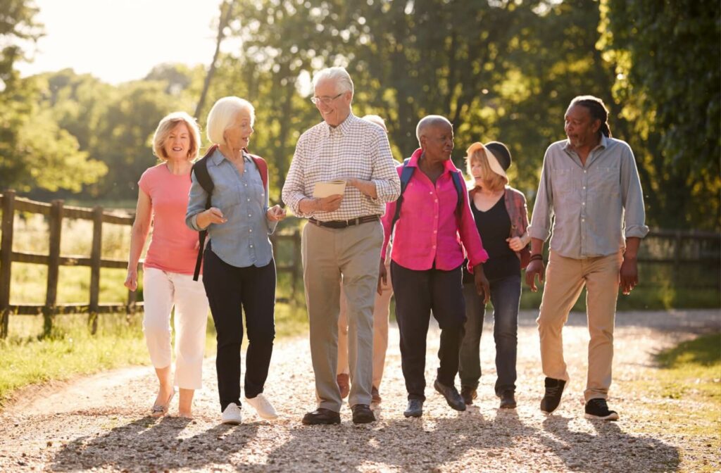 Group of older adults, some with backpacks, walking and socializing together on a country road.