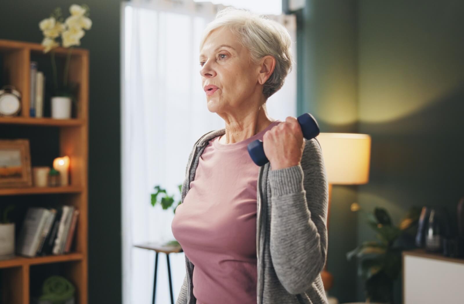 A senior breathes as they use a dumbbell to strengthen their arms.