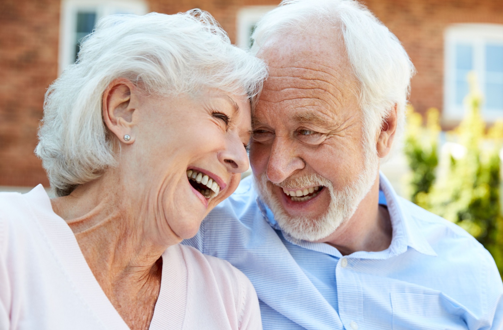 An older couple laugh while touching their foreheads together as they sit in the courtyard of their new senior living community