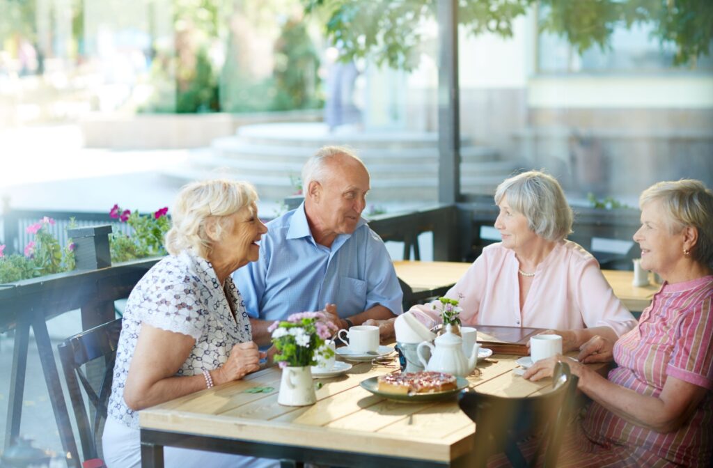 A group of 4 older adults sit on an outdoor patio while enjoying coffee and snacks in senior living