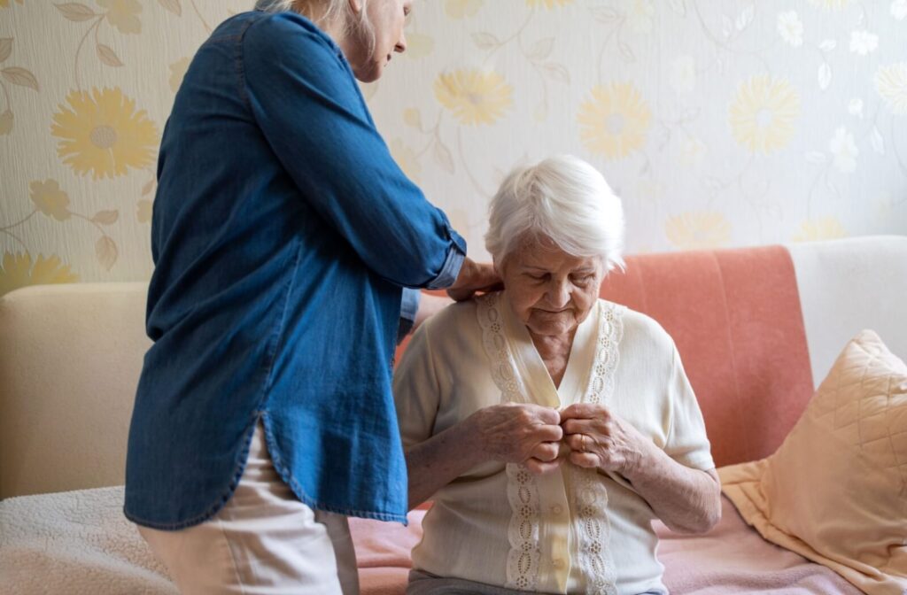 An older adult receives help with buttoning and adjusting their shirt from a supportive friend in memory care