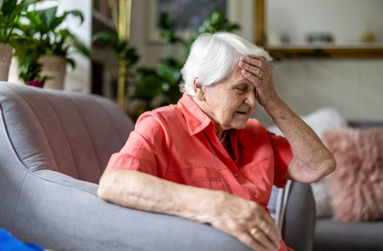 An older adult sits in an armchair and rubs their forehead in frustration due to their recent memory problems